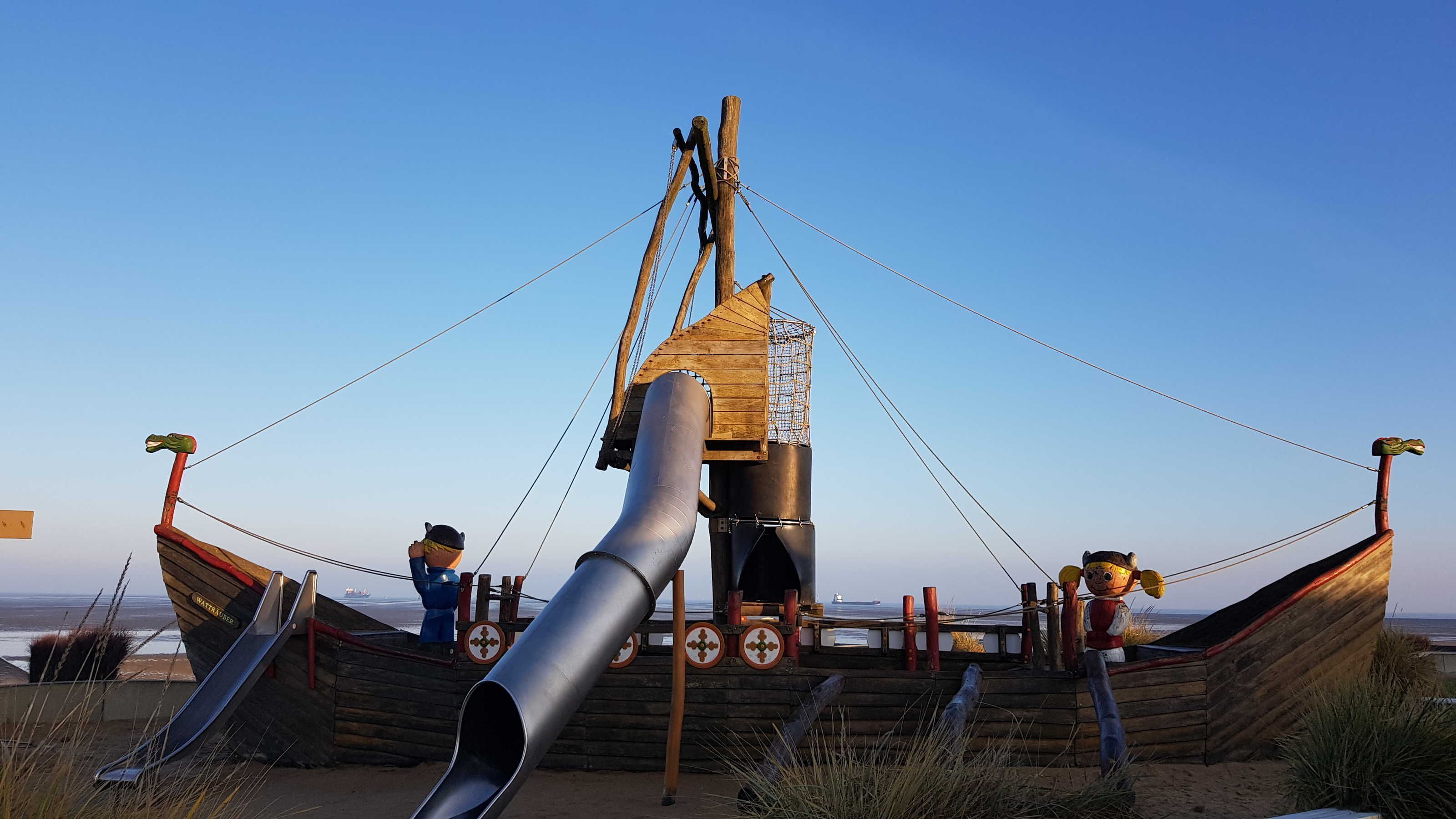 A wooden boat structure with a slide, a rope swing, and a netted enclosure.