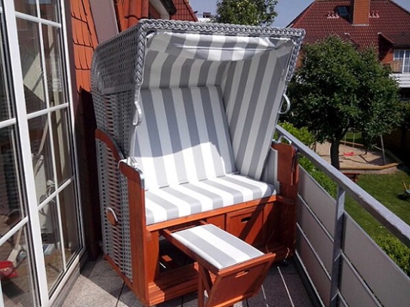 A wicker chair with a striped cushion and a wooden footrest on a balcony. - VOG-3.11 - Vogelsand 2 Apartment Complex (Cuxhaven)