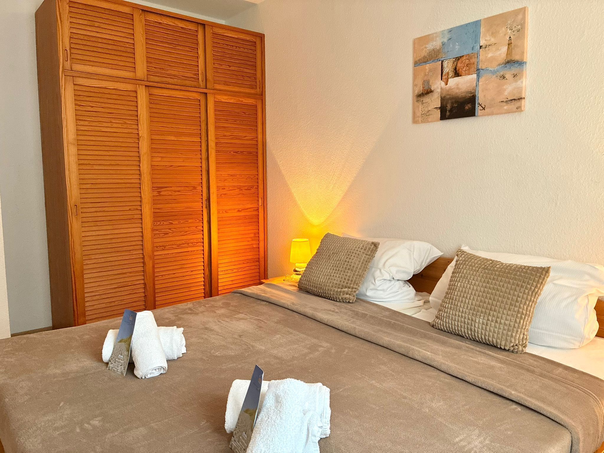 Habitación de hotel con un armario de madera grande, cama con ropa de cama blanca y un cuadro en la pared.