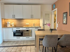 A modern kitchen with white cabinets, a wooden countertop, and a dining area with a table and chairs.
