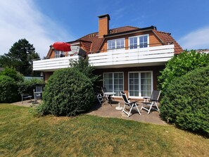 A two-story house with a balcony, a patio with outdoor furniture, and a well-maintained lawn.