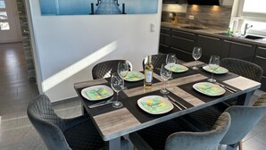 Een eethoek met een houten tafel gedekt voor zes personen, met borden met een groen en geel dessin, wijnglazen en een fles wijn.