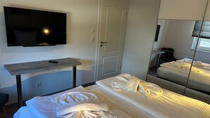 Een hotelkamer met een bed, een aan de muur bevestigde televisie, een klein tafeltje en een deur.