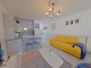 Un espacio habitable compacto con kitchenette, un sofá amarillo, una mesa de comedor con sillas y una pequeña mesa de centro.
