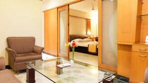 A hotel room with a glass coffee table, a brown armchair, a bed with a beige blanket, and a wooden cabinet. - Southern Crest (Chennai)