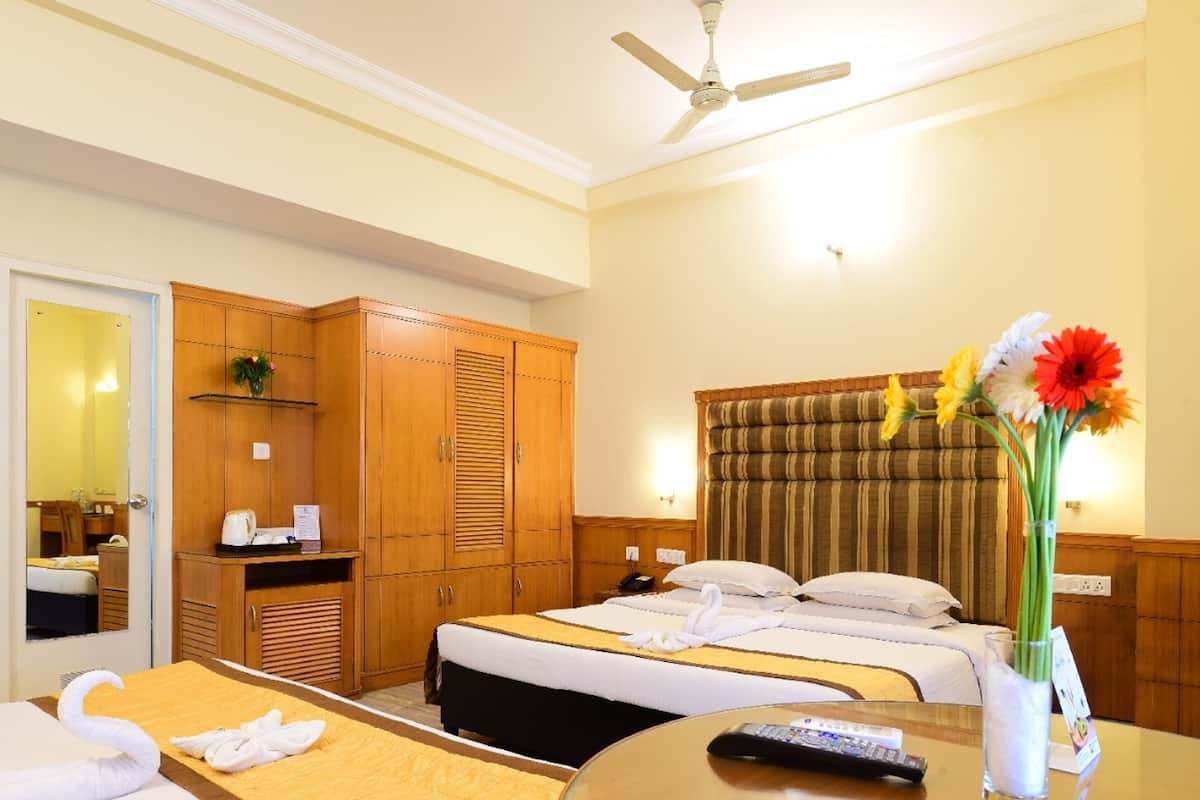 A hotel room with a bed, a desk, a chair, a wardrobe, a mirror, and a ceiling fan.