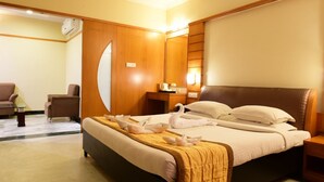 A hotel room with a large bed, a wooden wardrobe, a desk with a lamp, and a chair. - Southern Crest (Chennai)