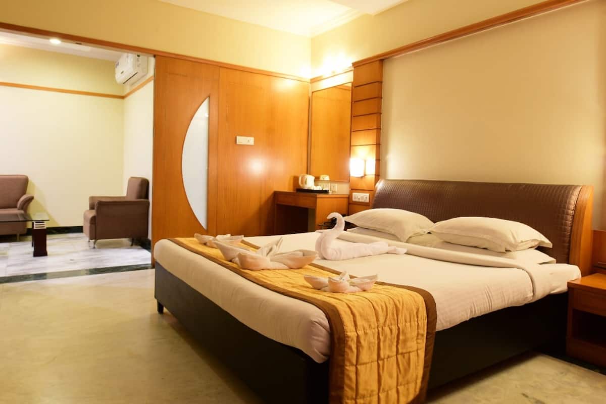A hotel room with a large bed, a wooden wardrobe, a desk with a lamp, and a chair.