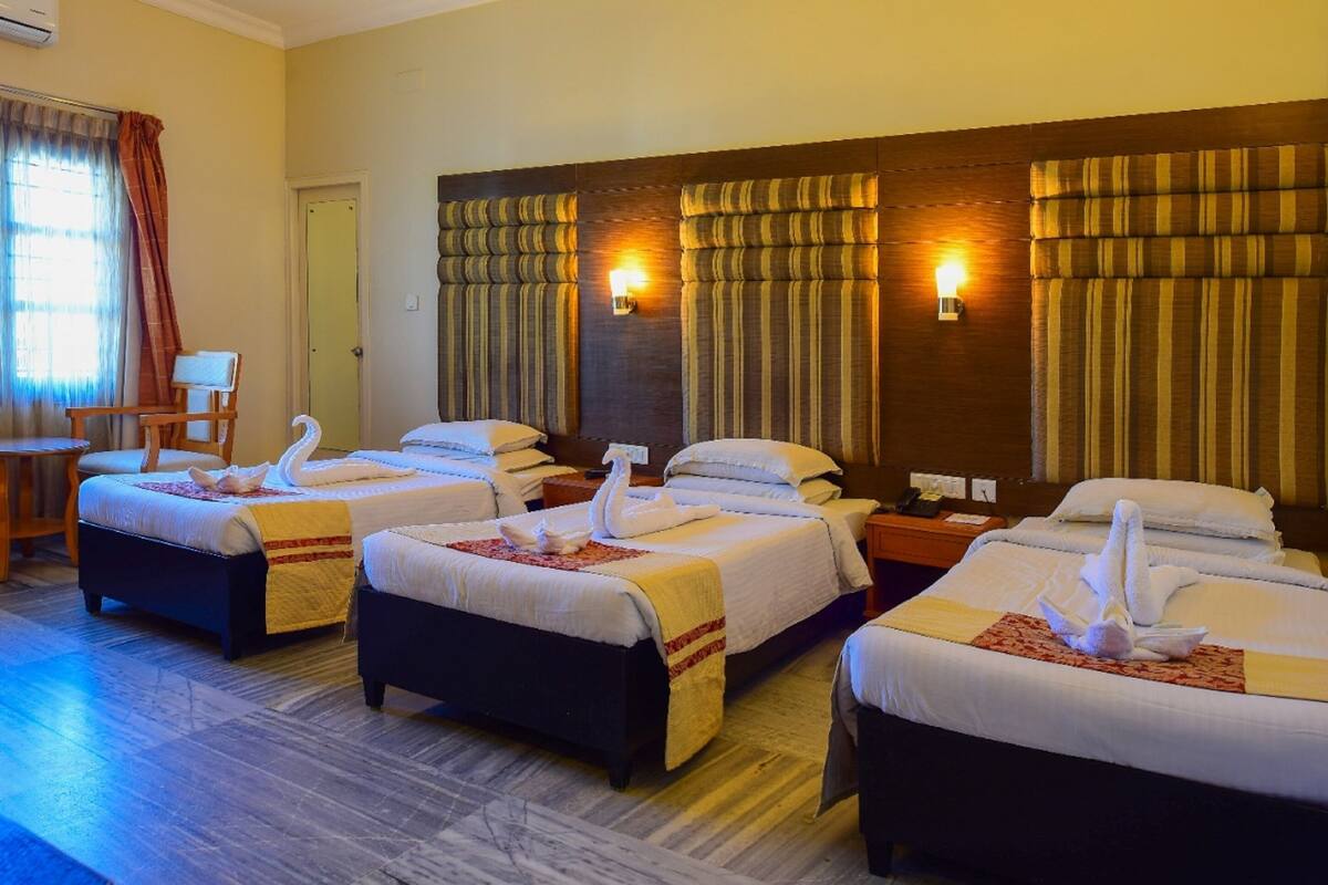 A hotel room with four beds, each with a swan towel arrangement, a wooden headboard, and a wall-mounted lamp.