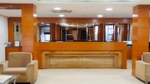 A lobby with a reception desk, two armchairs, and a small table. - Southern Crest (Chennai)