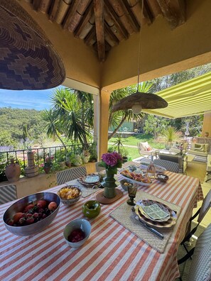 A dining area with a table set for a meal, surrounded by potted plants and outdoor furniture.