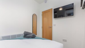 Una camera da letto con un letto, una porta in legno, una TV a parete e una parete bianca.