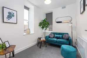 A modern living room with a teal sofa, a small side table with a plant, a framed picture, and a floor lamp.