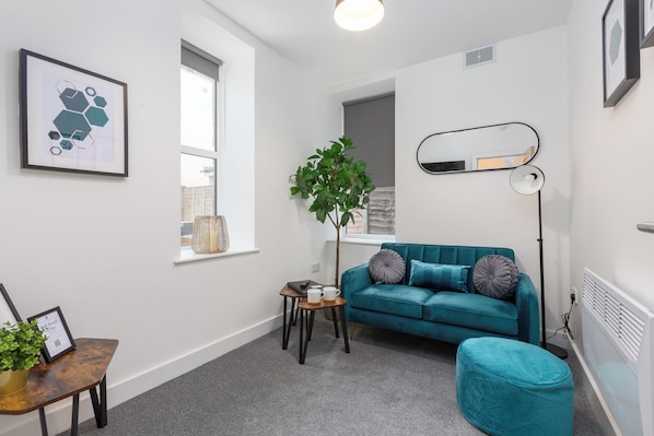 Un salon moderne avec un canapé de couleur turquoise, une petite table d’appoint ornée d’une plante, un tableau encadré et un lampadaire.