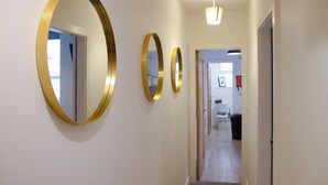 Un corridoio con tre specchi dorati appesi al muro, un lampadario sopra e una porta che dà su un bagno.