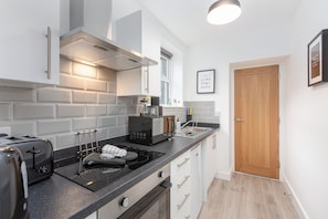 Une cuisine moderne équipée d’un grille-pain, d’une bouilloire et d’une cuisinière électrique noire. On y trouve une porte en bois et un tableau encadré au mur.