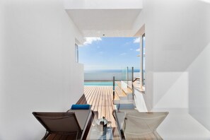 A modern room with a view of the sea, a wooden deck, and a glass table with a wine glass. - Suite Isabela (Lanzarote)