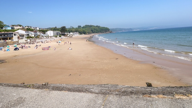 A wide sandy beach with people and tents, a clear blue sky, and buildings along the coastline. - 13 Lyndhurst Avenue (Kilgetty)