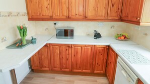 A kitchen with wooden cabinets, a microwave, a fruit bowl, and a green vase with tulips. - 13 Lyndhurst Avenue (Kilgetty)