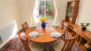 A dining area with a round wooden table set for four, surrounded by wooden chairs. A vase with yellow flowers is placed on the table. - 13 Lyndhurst Avenue (Kilgetty)