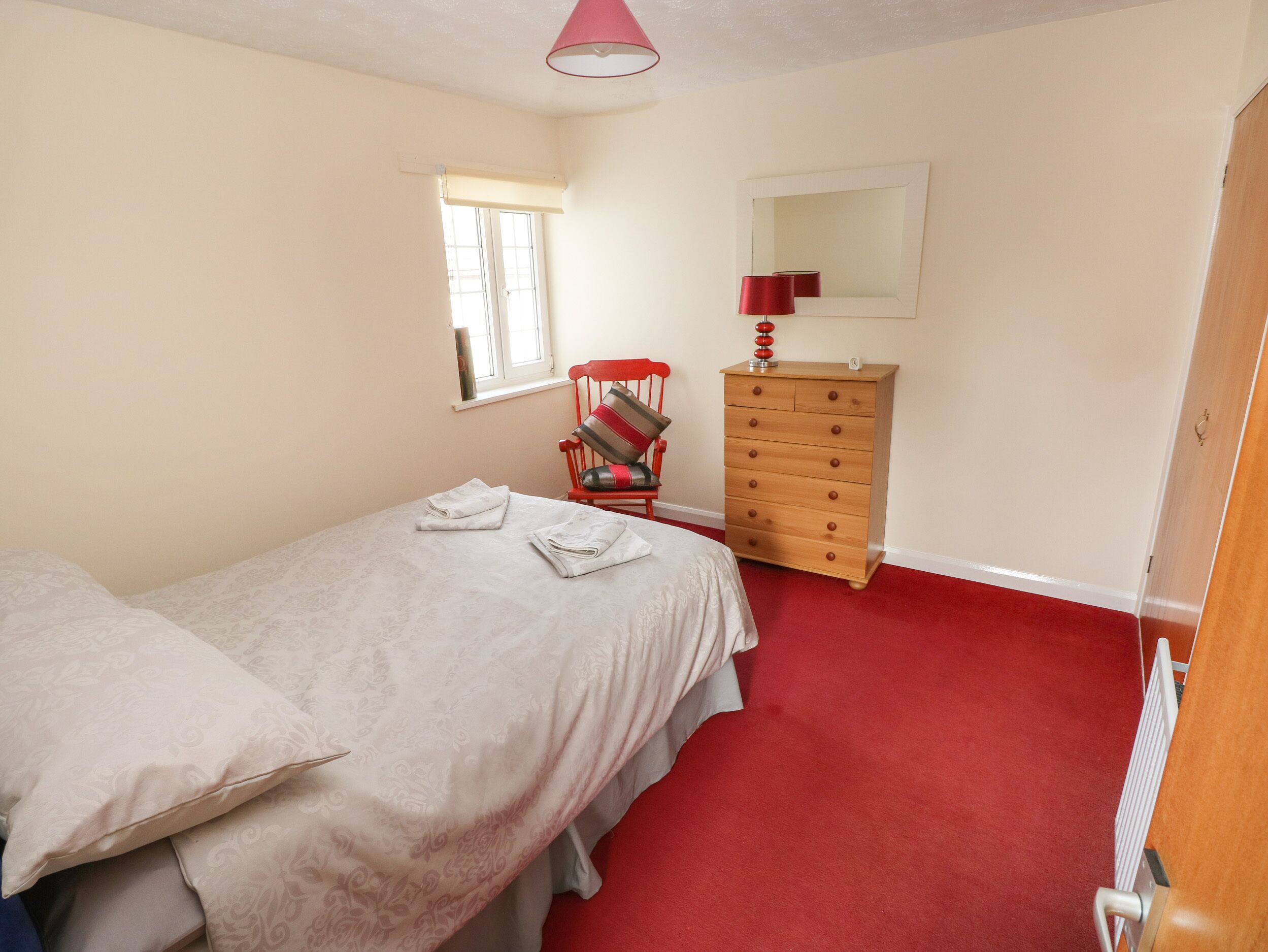 A bedroom with a bed, a dresser, a chair, a window, and a mirror.