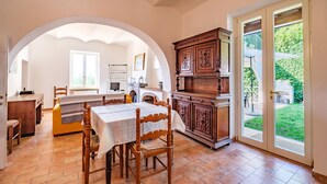 A dining area with a table set for four, a wooden cabinet, and a view of a garden through a glass door. - APARTMENT 6 PEOPLE IN COUNTRY VILLA WITH POOL (Lame)