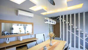 A modern dining area with a wooden table, chairs, a vase with dried plants, and a large mirror above the table. - Design Villa Nicol Heated Pool Seaview (Malevizi)