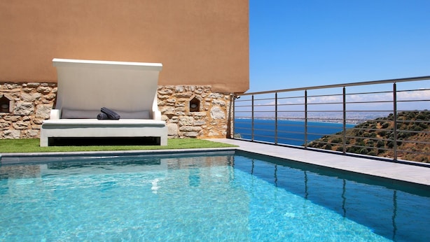 A pool area with a lounge chair, a stone wall, and a view of the sea. - Design Villa Nicol Heated Pool Seaview (Malevizi)
