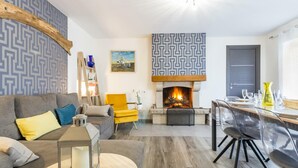 A modern living room with a fireplace, a dining area, and a patterned wall. - Charming house in Granville with garden and terrace (Granville)