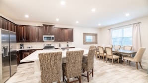 A modern kitchen with dark wood cabinets, a stainless steel refrigerator, a microwave, and a large island with chairs. - Chic Home near Disney: Private Pool, Game Room & Waterpark - 320AU (Kissimmee)