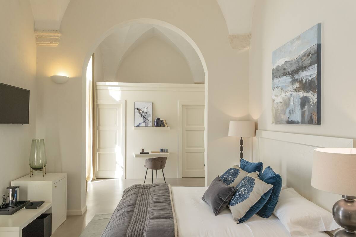 A bedroom with a bed, bedside table, lamp, and artwork on the wall.