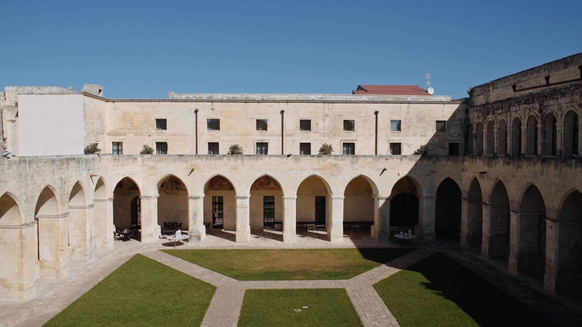 Une cour intérieure avec une pelouse centrale, entourée d’un bâtiment doté de nombreuses arcades et d’un toit plat.