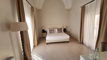A hotel room with a large bed, two bedside tables with lamps, a radiator, and a desk with a bottle.