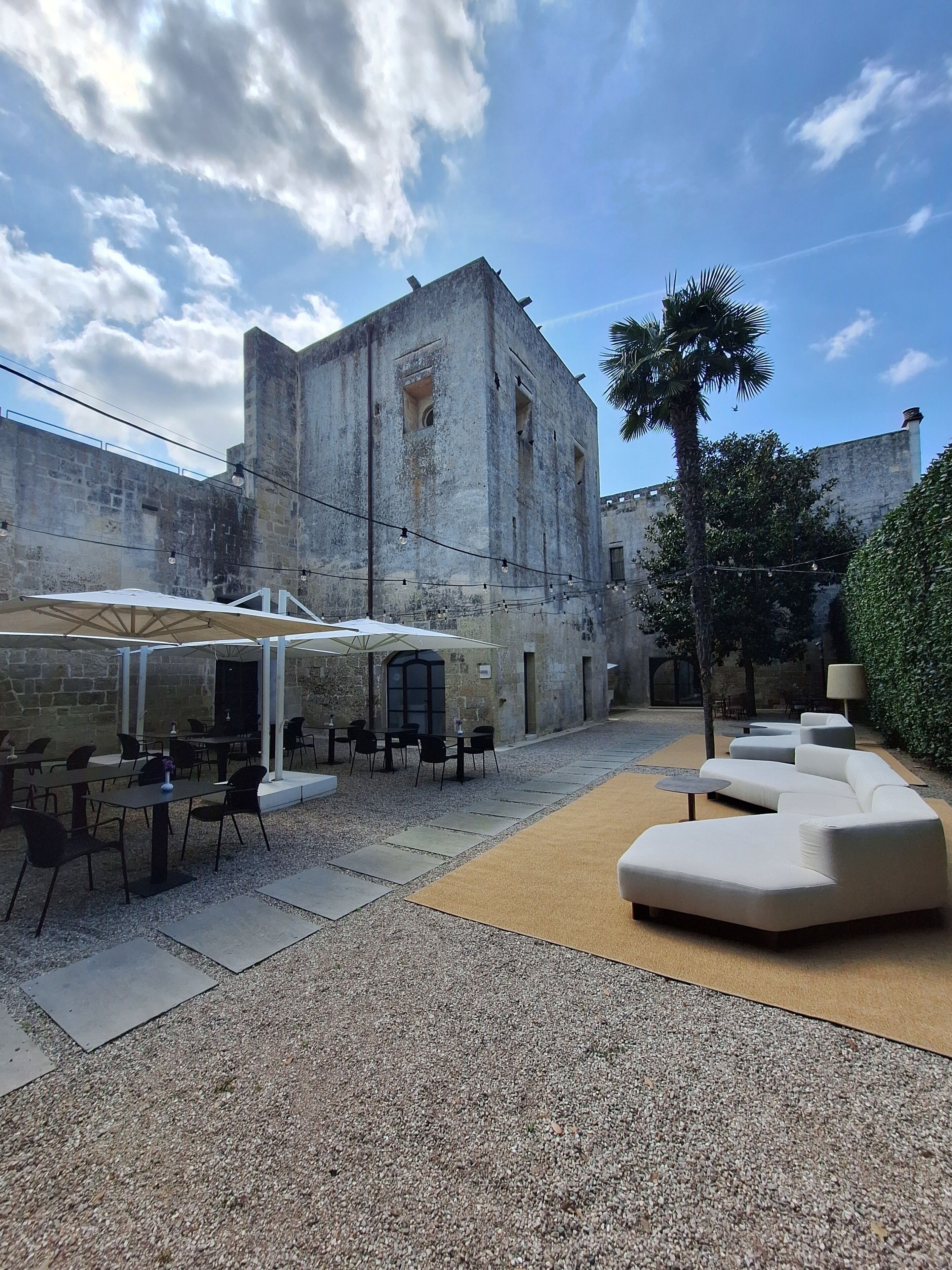 An outdoor seating area with tables and chairs, a white umbrella, and a modern sofa.