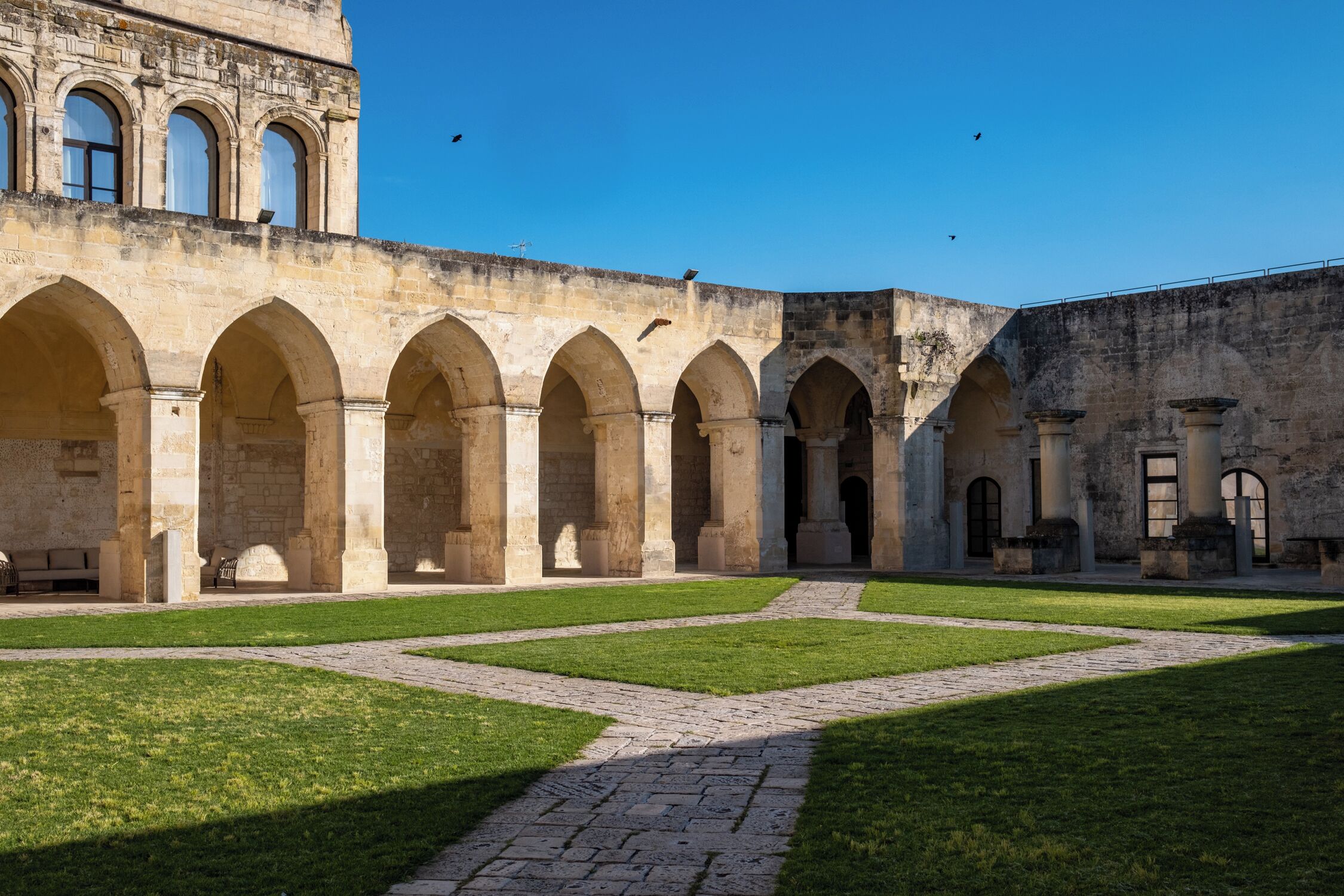Ein alter Innenhof mit steinernen Bögen, einem gepflasterten Weg und einer Rasenfläche.