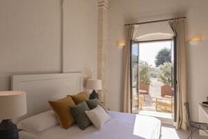 Una habitación de hotel con una cama, dos lámparas de noche, una ventana con cortinas y vistas al área de asientos exteriores.
