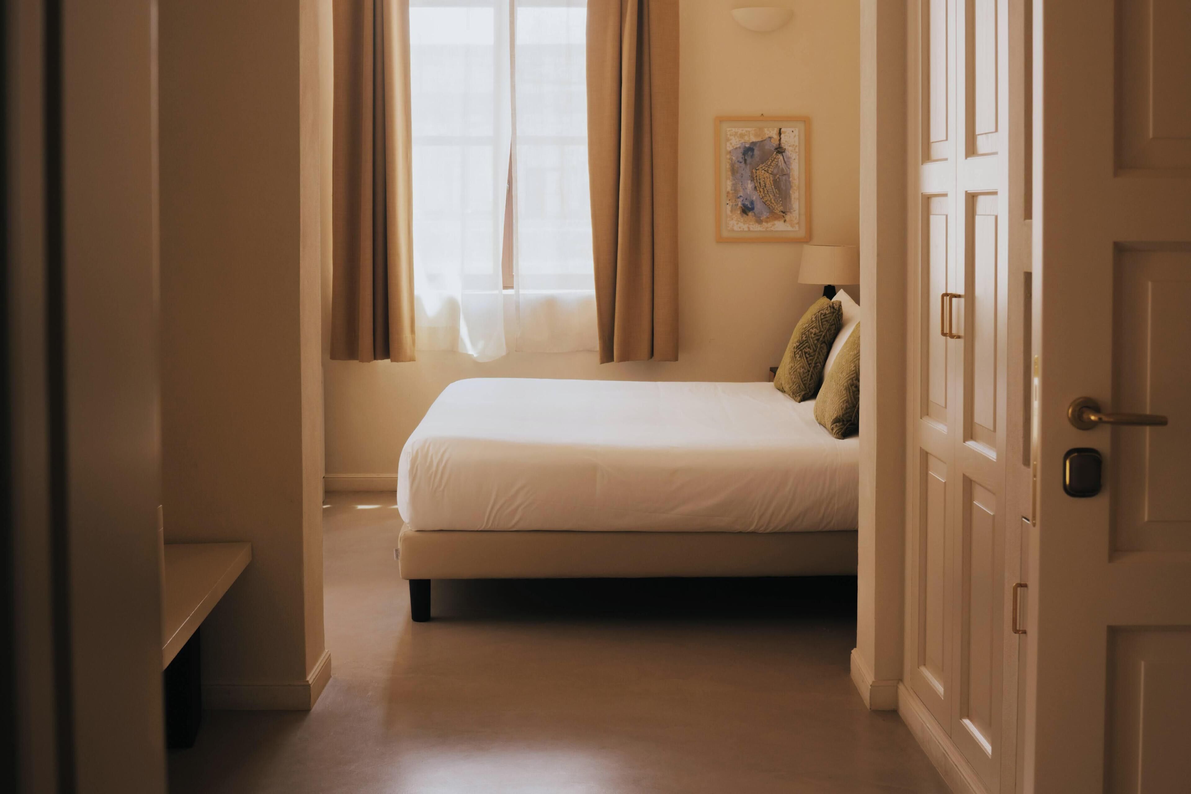 Un dormitorio con cama, ventana con cortinas, un cuadro en la pared y una puerta con cerradura.