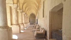 Un pasillo con arcos, columnas y zonas de estar, que sugiere un edificio histórico o religioso.