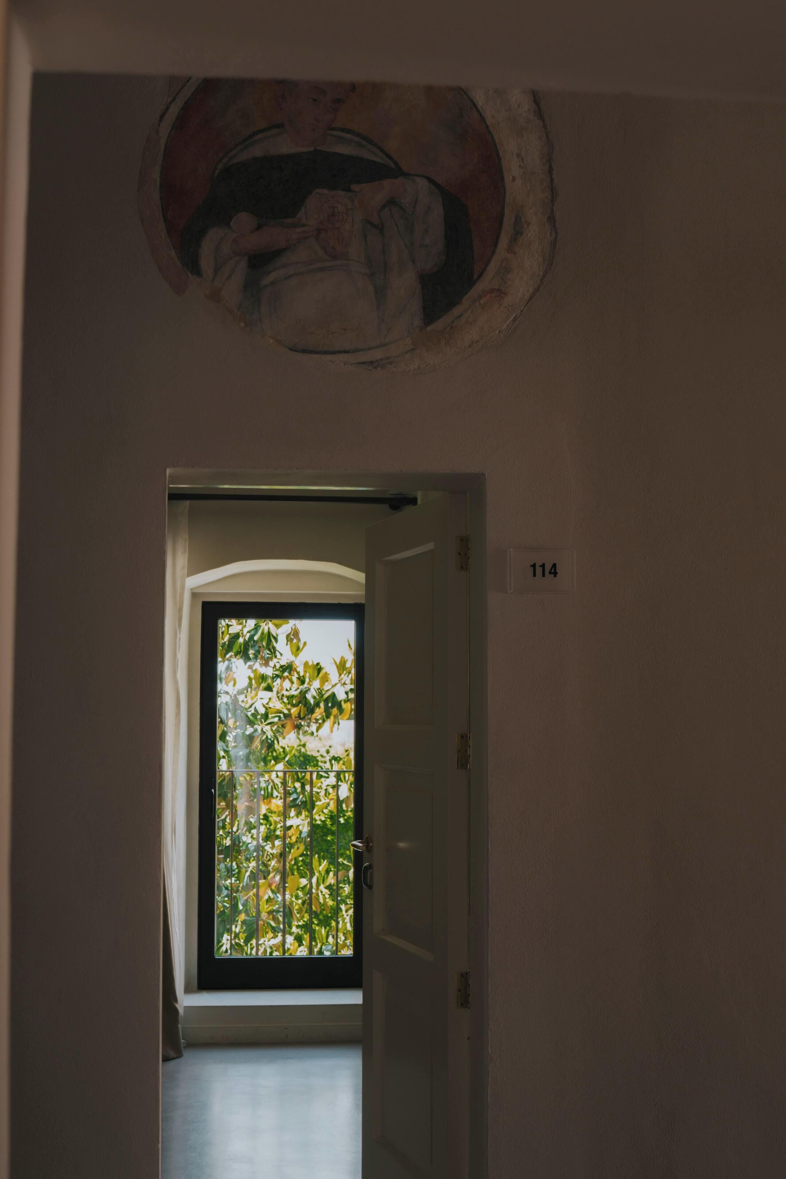 A hallway with a door labeled '114' leading to a balcony with a view of trees.