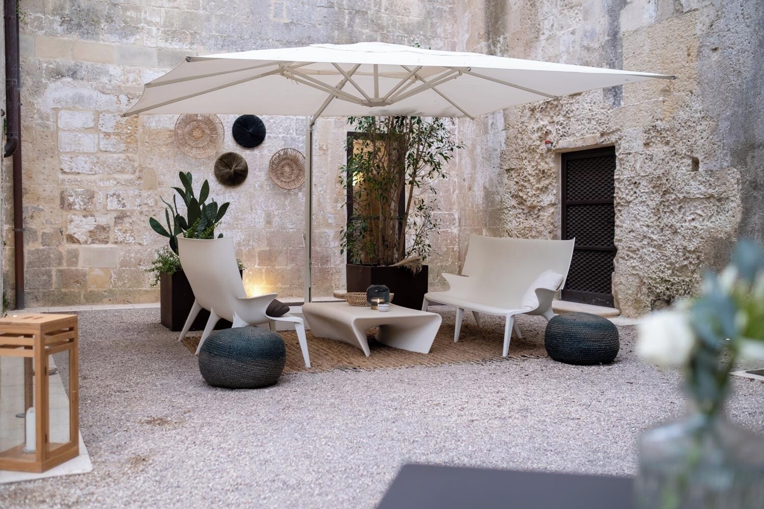 An outdoor seating area with a white umbrella, stone walls, and potted plants.