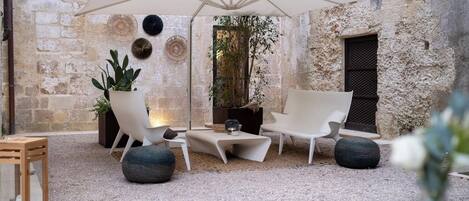 An outdoor seating area with a white umbrella, stone walls, and potted plants.