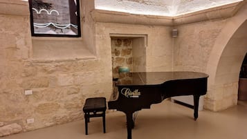 A grand piano in a spacious room with stone walls and an arched doorway.
