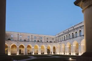 Un patio con múltiples arcos y columnas, un espacio central abierto y la fachada de un edificio con ventanas.