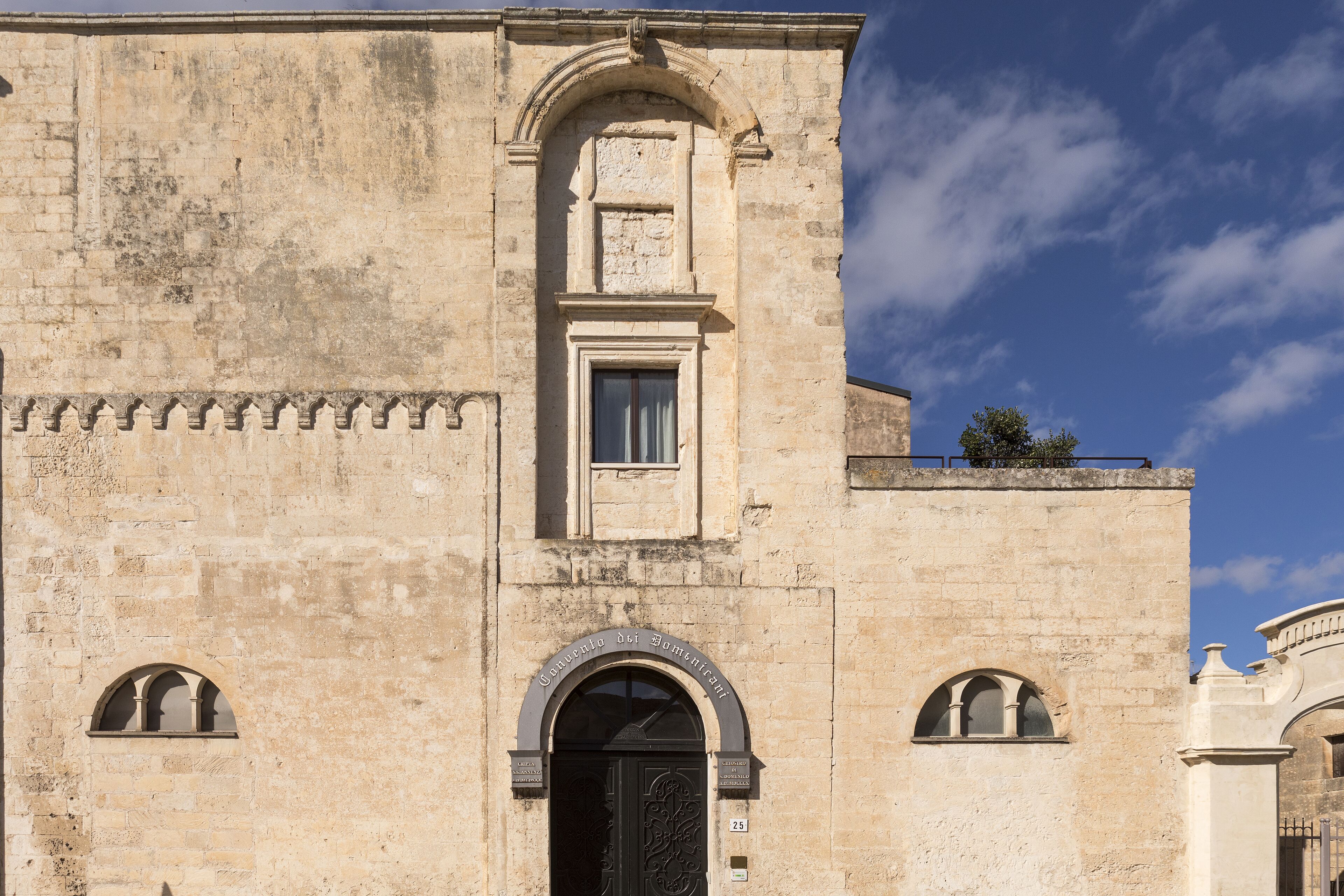 A historic building with a central arched entrance, a small window above the door, and a balcony with a railing.