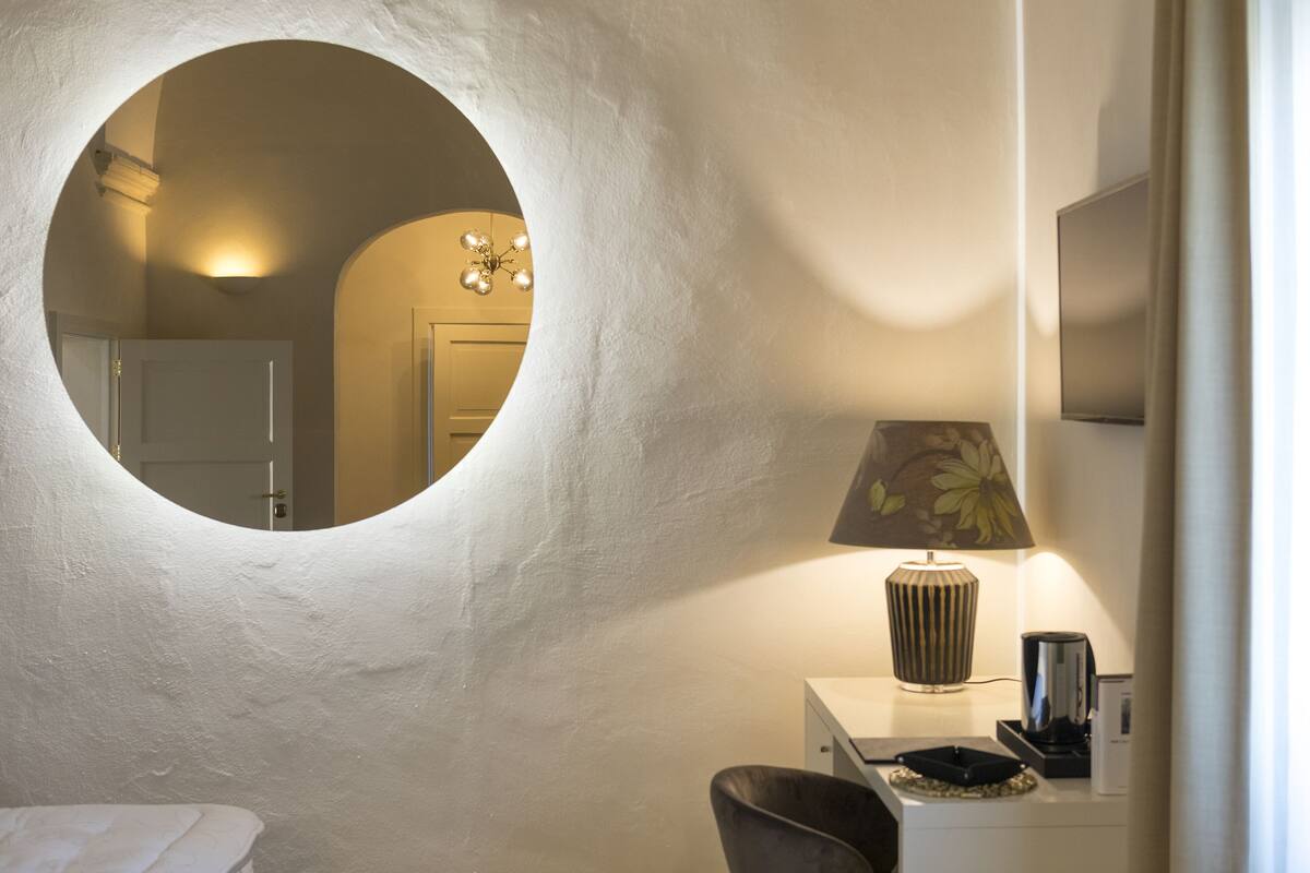 A room with a round mirror, a lamp, a chair, and a small table.
