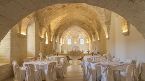 Un comedor abovedado con mesas dispuestas para una comida, paredes de piedra y luz natural proveniente de ventanas.