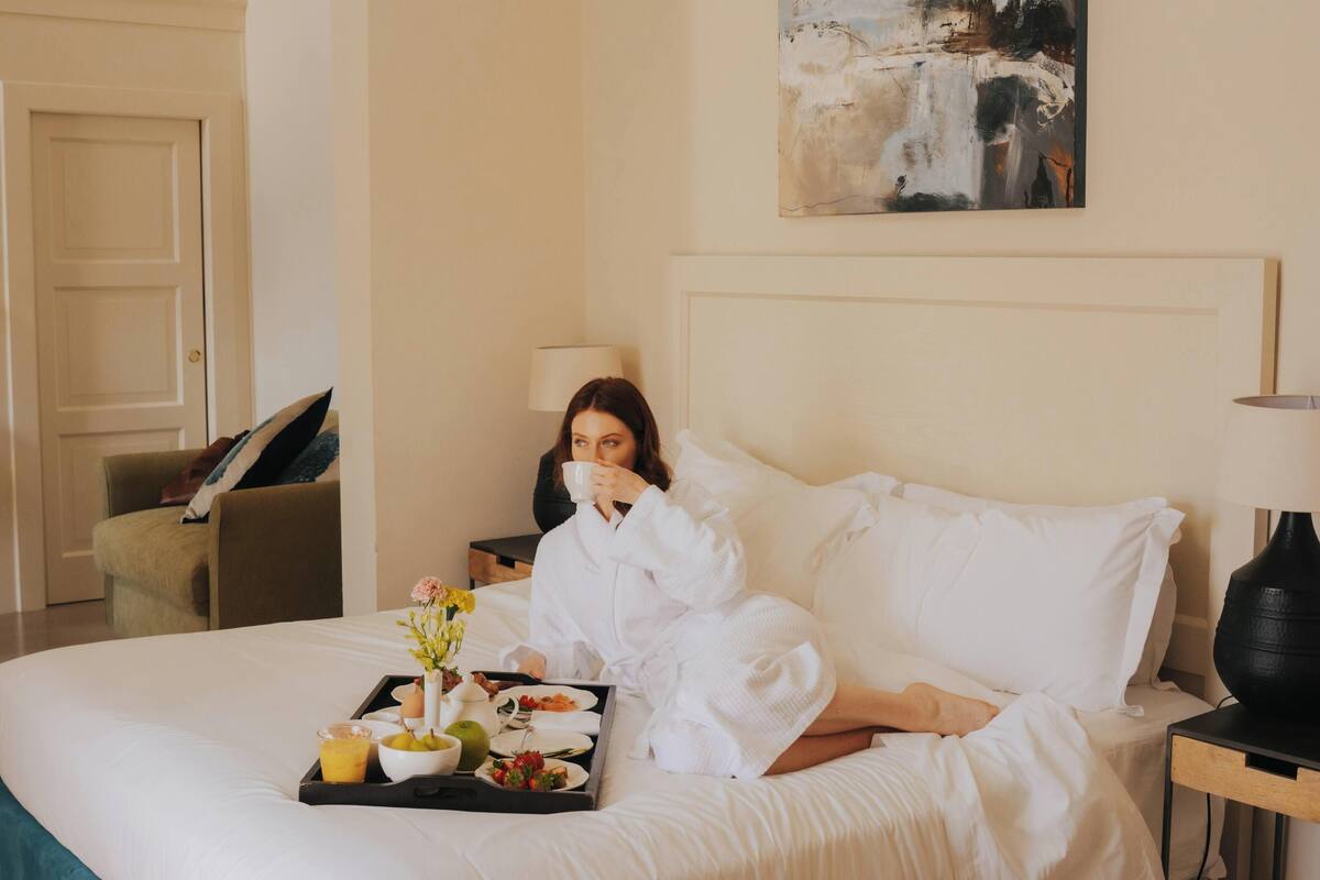 A hotel room with a bed, a bedside table, a lamp, a painting on the wall, and a chair.