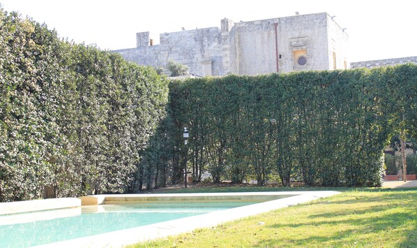 Una piscina con setos y un edificio al fondo.