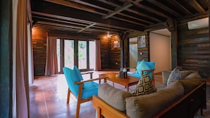 Habitación acogedora con vigas de madera, un sofá, dos sillones, una mesita y vistas a través de un ventanal.