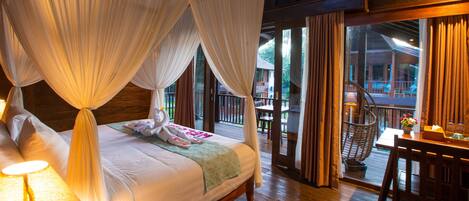 A bedroom with a canopy bed, wooden flooring, and a view of the outdoor area.